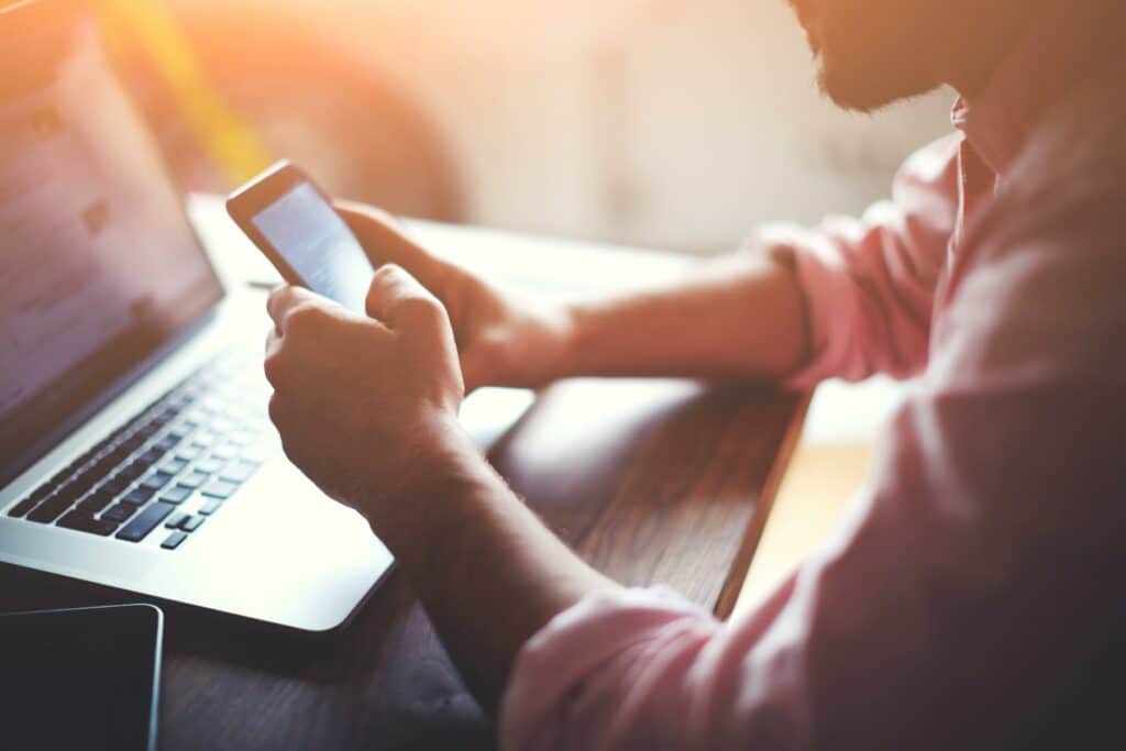 A man is using phone infornt of laptop