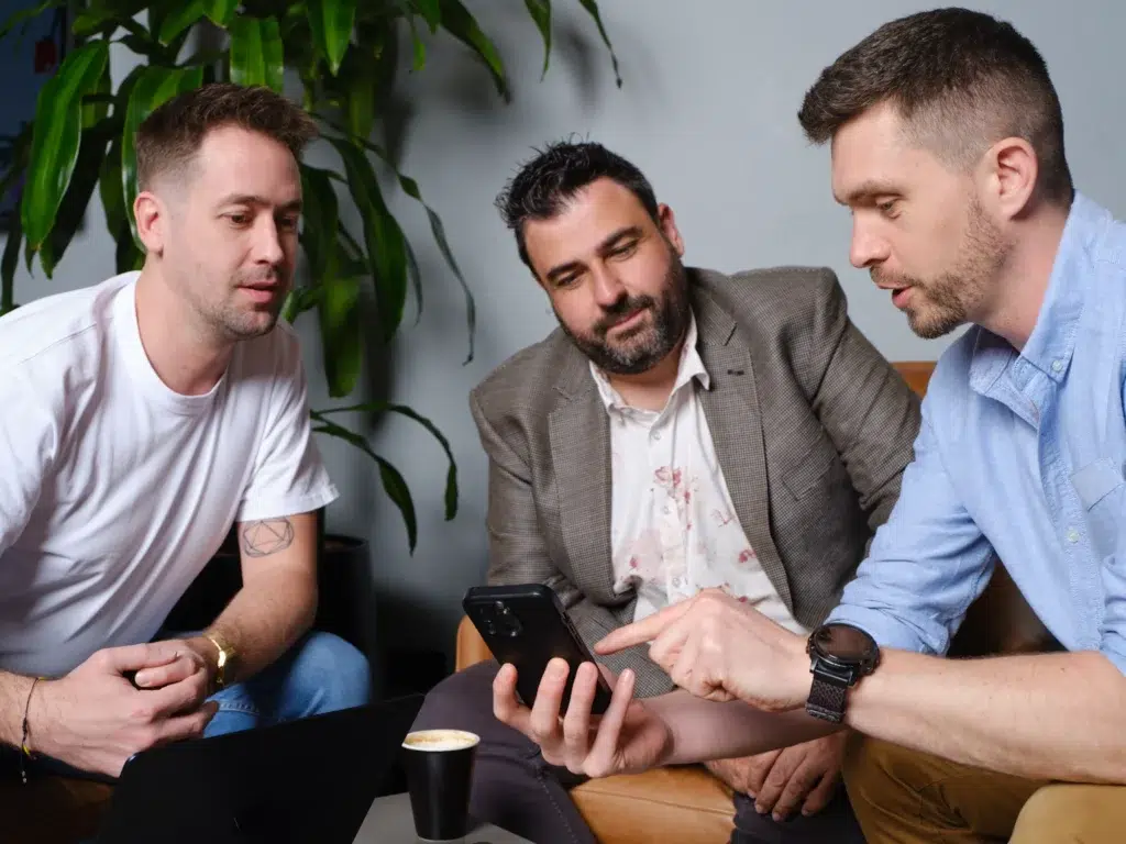 Simon showing a phone to James and Ray