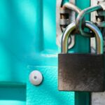 Close-up of a steel padlock locking the latch on a bright teal door
