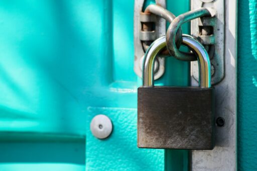 Close-up of a steel padlock locking the latch on a bright teal door